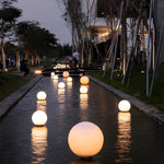 Large illuminated orb lights lining wet pathway creating stunning reflective lighting design at dusk