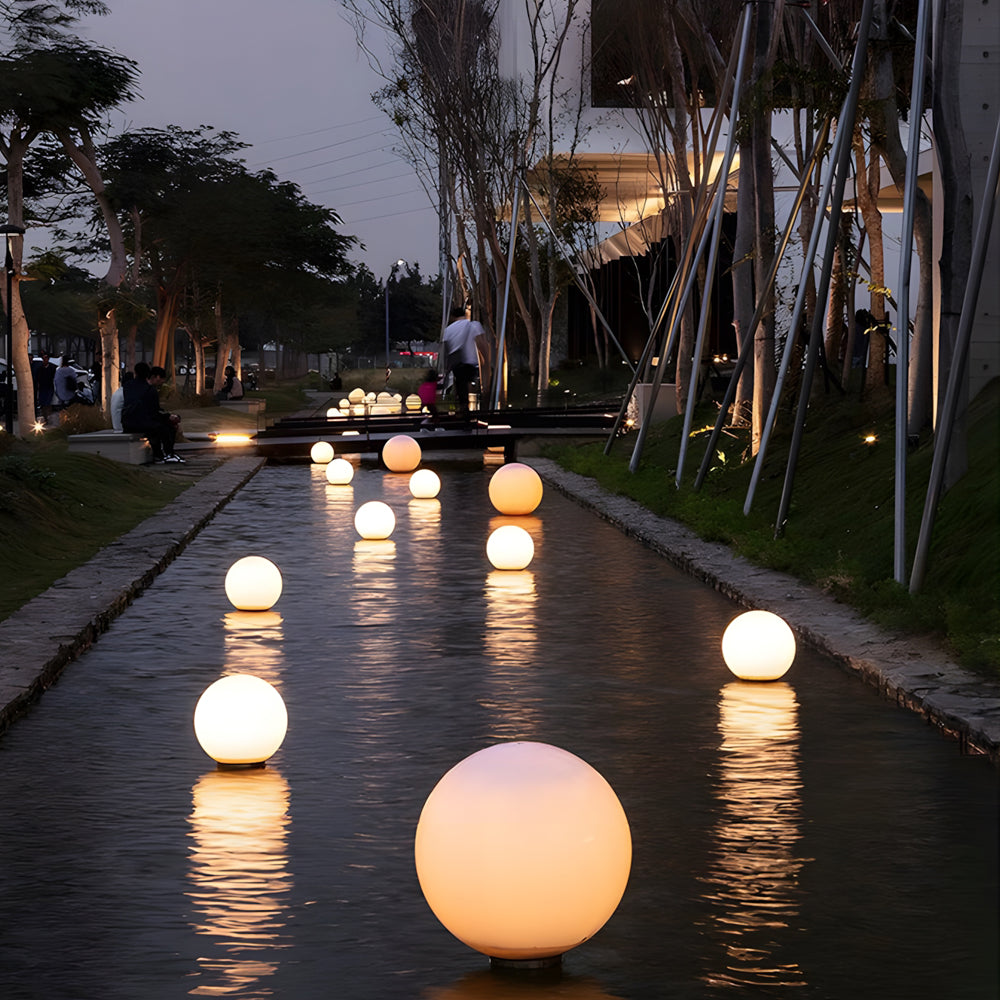 Large illuminated orb lights lining wet pathway creating stunning reflective lighting design at dusk