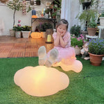 Child playing on grass beside glowing organic-shaped outdoor light fixture during golden hour