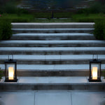 Two matching outdoor lanterns with LED candles illuminating concrete steps during twilight hours