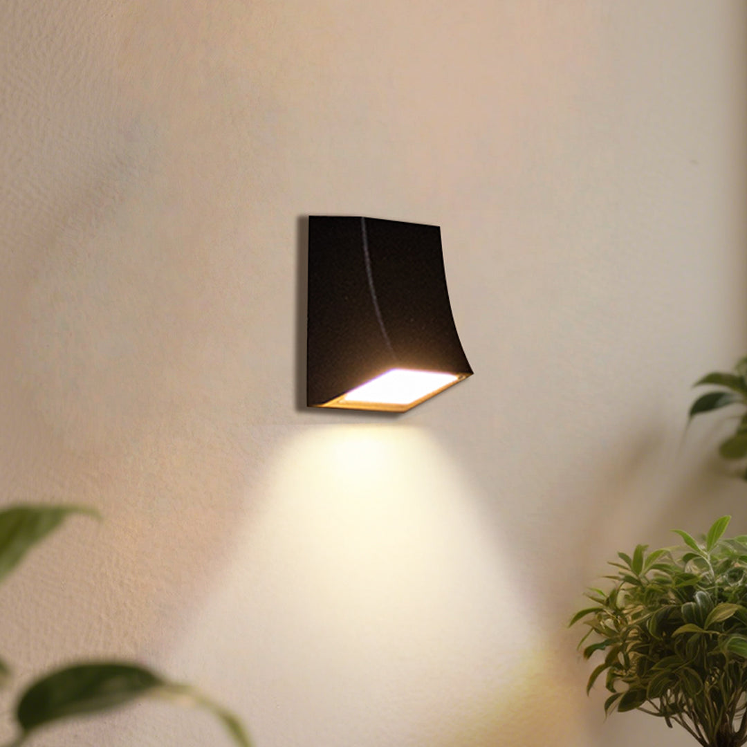 Contemporary black wall light illuminating textured stone surface with dramatic shadows