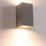 Contemporary square wall sconce creating warm downward light beam on exterior building surface