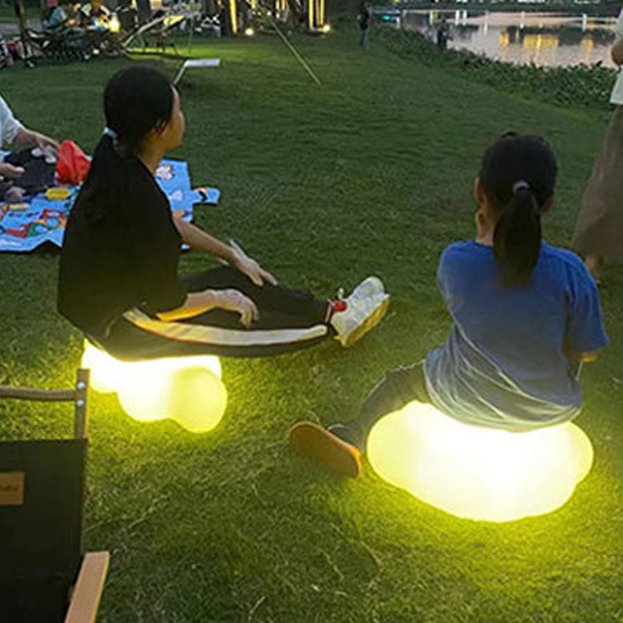 Two people relaxing on grass with illuminated cloud-shaped outdoor lights creating ambient evening atmosphere