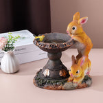 Multi-rabbit fountain display with ornate water basin and butterfly accents on neutral background