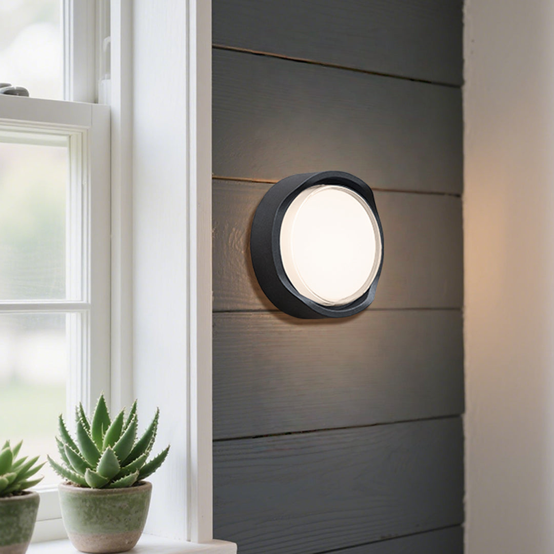 Round outdoor wall sconce with frosted diffuser creating ambient lighting on building exterior