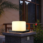Cube-shaped LED light providing soft illumination on textured outdoor table with tropical plants nearby