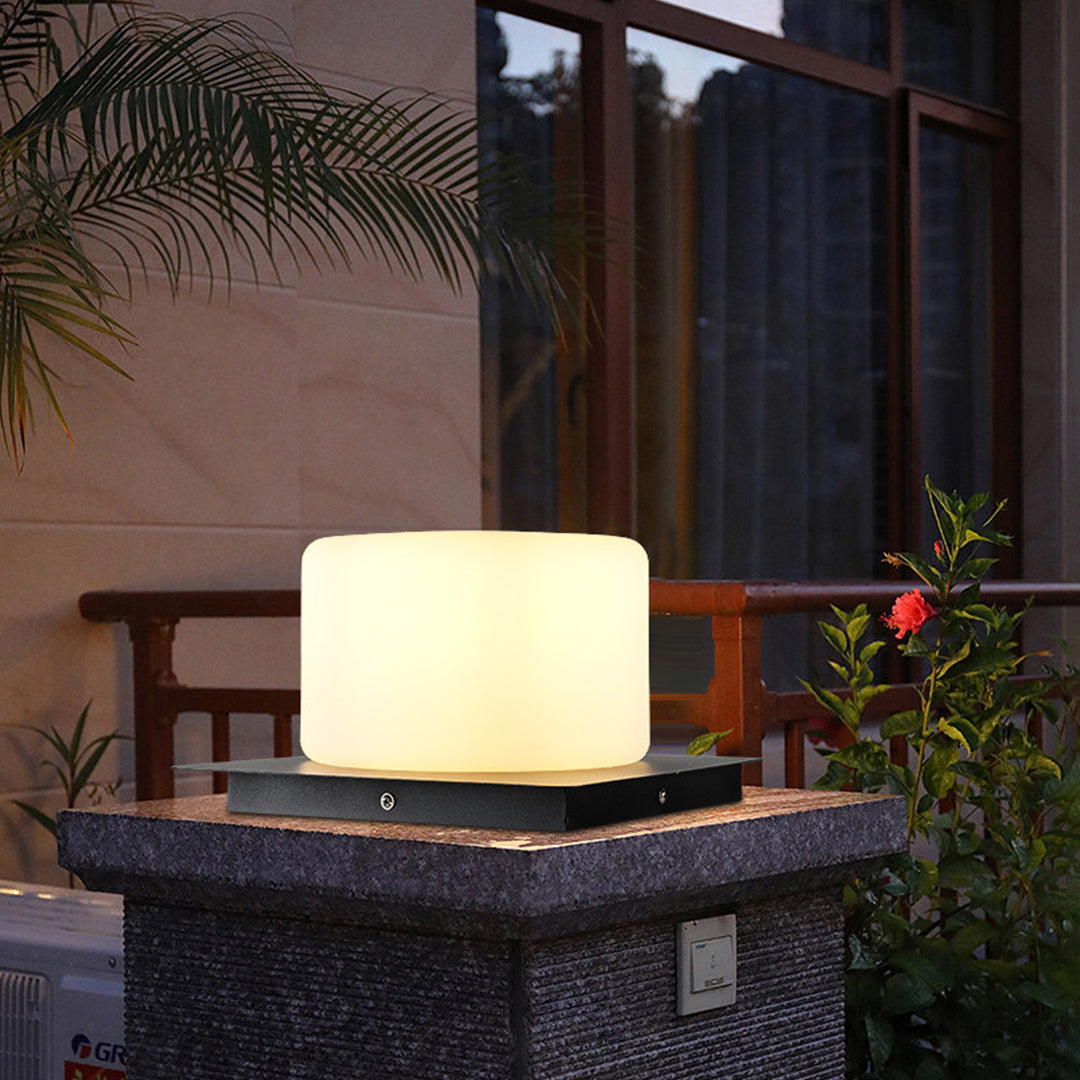 Cube-shaped LED light providing soft illumination on textured outdoor table with tropical plants nearby