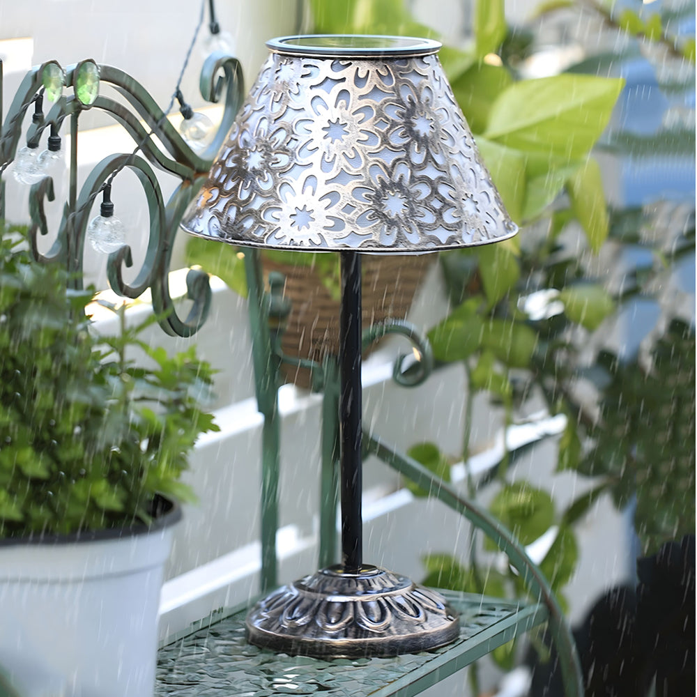 Elegant outdoor solar lamp with filigree shade positioned on patio table beside lush greenery