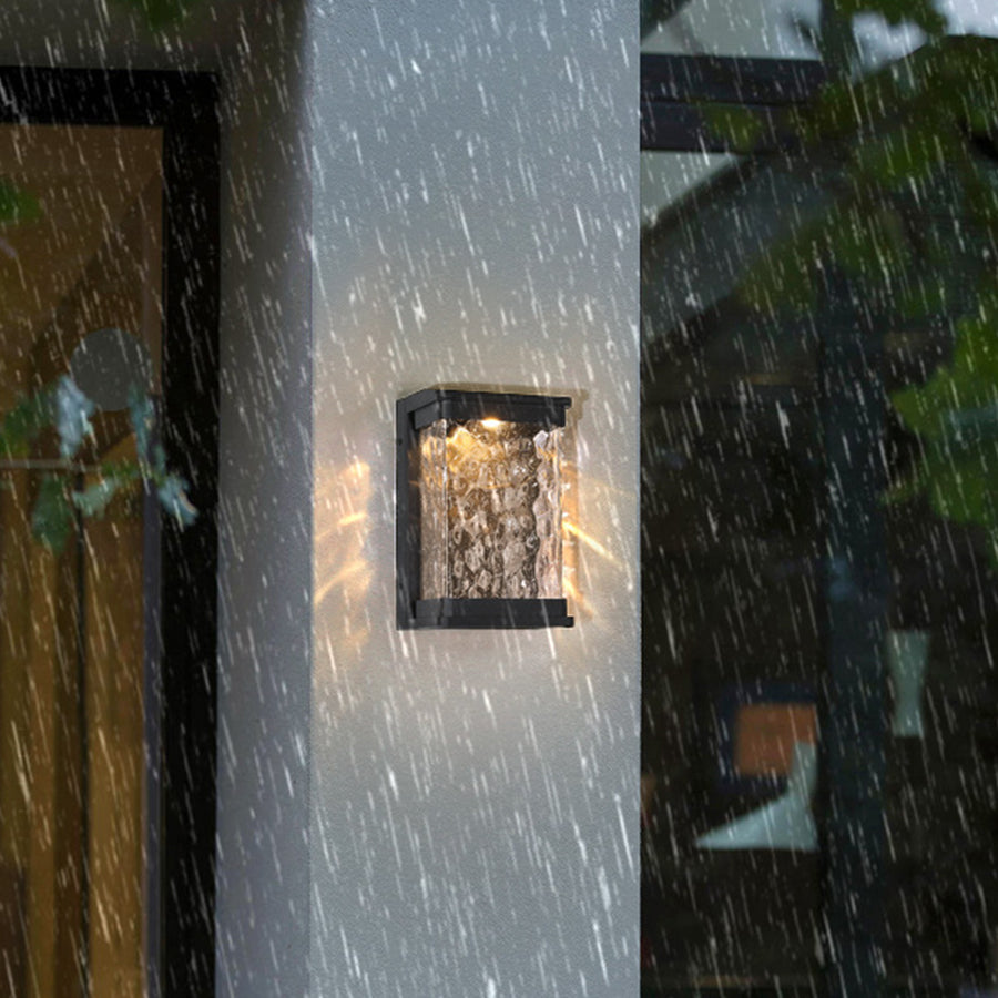 Modern black outdoor wall sconce with bubble glass creating dramatic lighting on stone exterior