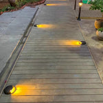 Circular in-ground fixture with angled light output designed for pathway and accent lighting