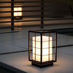 Square lantern with grid pattern illuminating concrete patio area at nighttime