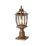 Traditional bronze pillar light with ornate decorative base and clear glass lantern top featuring warm illumination
